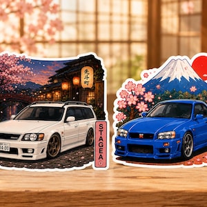May include: Two die-cut stickers featuring Japanese sports cars. The left sticker shows a white station wagon with the text STAGEA, and the right sticker shows a blue coupe with Mount Fuji, cherry blossoms, and the text R34 in Japanese characters.