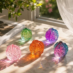 May include: Five translucent glass ornaments shaped like walnuts, each featuring a distinct vibrant color including pink, green, orange, purple, and a multi-colored blue and purple blend, all displaying a textured, faceted surface finish.