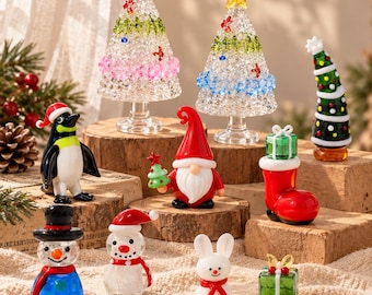 Könnte beinhalten: Eine Sammlung von Miniatur-Weihnachtsfiguren aus Glas, darunter zwei klare, strukturierte Bäume mit gelben Sternen, ein Pinguin, ein Wichtel, ein roter Stiefel mit Geschenk, ein grüner Baum, ein Schneemann, ein kleinerer Schneemann, ein Hase und ein Geschenk.