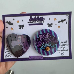 Puede incluir: Un botón en forma de corazón con un personaje de piel morada y cabello blanco, y un botón circular con rayas moradas y azules, el texto "Poor Unfortunate Soul" y un pequeño gráfico de concha, montados en una tarjeta blanca.