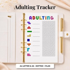 Può includere: Un raccoglitore bianco a sei anelli contenente una pagina di pianificazione intitolata Adulting Tracker. La pagina presenta grafiche a blocchi in stile pixel colorati, linee orizzontali per scrivere e una sezione a griglia. Una penna dorata è fissata sul lato.