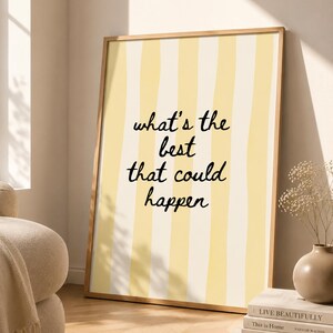 May include: A rectangular wall art print in a light wooden frame featuring vertical pale yellow stripes and the black handwritten text what's the best that could happen centred on the surface. The design is clean and simple with a light colour palette.