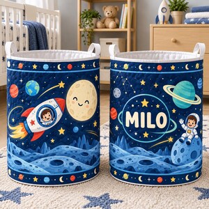 May include: Two cylindrical fabric storage baskets featuring a dark blue space theme with quilted texture. The design includes planets, stars, a rocket ship with a pilot, a smiling moon, and an astronaut sitting on a cratered moon with the name MILO.