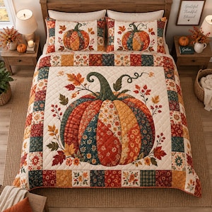 May include: A quilted bedspread and two matching pillow shams featuring a large central pumpkin graphic composed of various floral and plaid fabric patches in autumn colours, surrounded by fall leaves, with a patchwork border of squares.