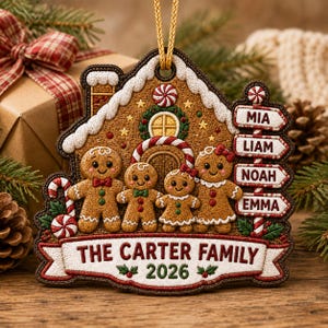 Op de afbeelding: Een peperkoekhuis-ornament met vier peperkoekfiguren, een wegwijzer met de namen Mia, Liam, Noah en Emma, en een banner onderaan met de tekst The Carter Family 2026. Het ontwerp bevat zuurstokken en wit glazuur.