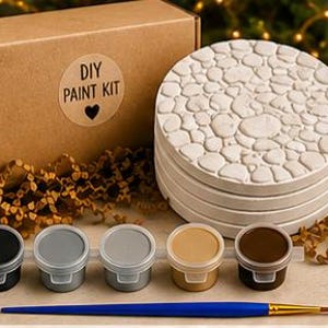 May include: A DIY paint kit featuring a brown cardboard box with a circular sticker labeled DIY PAINT KIT with a heart icon, a stack of four round white stone-textured coasters, five small paint pots in black, gray, and brown, and a blue paintbrush.