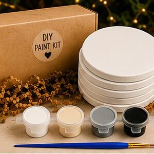 Pode incluir: Um kit de pintura DIY com uma caixa de cartão castanha com um autocolante circular com a etiqueta DIY PAINT KIT e um ícone de coração, cinco bases para copos redondas em cerâmica branca, quatro pequenos potes de tinta e um pincel azul.