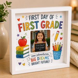 Puede incluir: Un marco cuadrado blanco que contiene la foto de un niño sosteniendo una pequeña pizarra. El marco presenta texto colorido FIRST DAY OF FIRST GRADE, new adventures, BIG DREAMS, BRIGHT FUTURE, con ilustraciones de libros, una manzana y lápices.