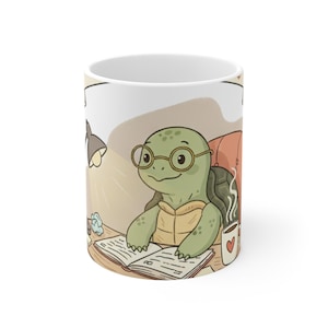 May include: A white ceramic mug featuring a cartoon illustration of a green turtle wearing round glasses, sitting at a desk with an open book, a desk lamp, and a small white mug with a red heart icon, all set against a soft beige background.
