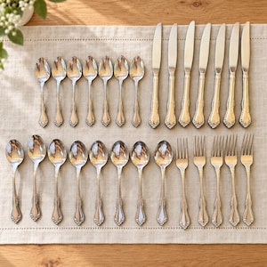 May include: A flatware set consisting of seven silver-toned dinner knives, fifteen silver-toned spoons of varying sizes, and five silver-toned forks. Each piece features a polished metallic finish and a decorative embossed pattern on the handle.
