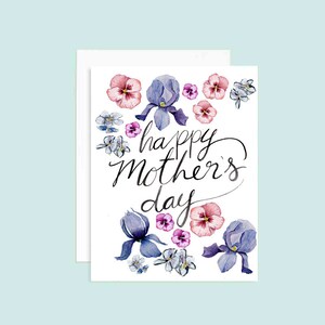 Puede incluir: Una tarjeta blanca con una ilustración de acuarela de flores moradas y rosas. El texto "happy mother's day" está escrito en caligrafía negra.