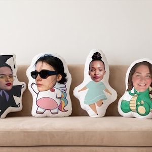 May include: Four custom-shaped throw pillows featuring printed photographic faces of different individuals. The designs include a person in a graduation gown, a person with sunglasses on a unicorn body, a person in a light blue dress, and a person on a green dinosaur.