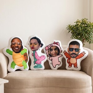 Pode incluir: Quatro almofadas de formato personalizado com corpos de desenhos animados impressos e rostos humanos realistas. Os designs incluem uma tartaruga, um personagem rosa, um porco com capuz e um macaco, cada um exibindo uma cabeça humana.