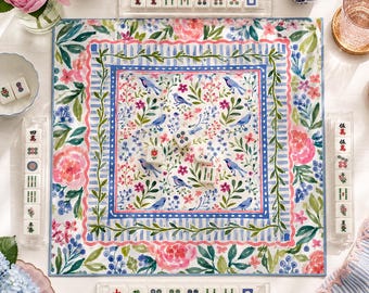 Può includere: Un tappetino da mahjong quadrato con un motivo floreale e di uccelli ad acquerello, con peonie rosa, uccelli blu e fogliame verde. Il tappetino è circondato da quattro supporti in acrilico trasparente contenenti tessere bianche da mahjong.