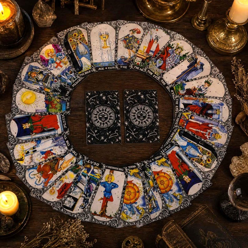 May include: A circular arrangement of tarot cards featuring colorful illustrations and black borders, surrounding two central cards with a black and white sun and star design. The cards display various figures, symbols, and text labels.