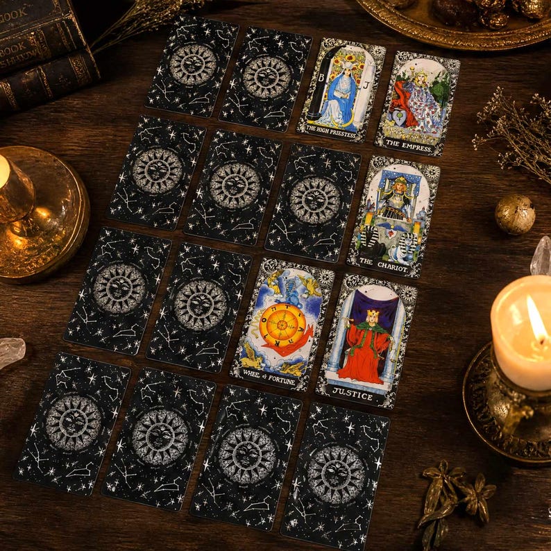 May include: A collection of tarot cards arranged in a grid on a dark wooden surface. The cards feature a black background with white celestial sun and constellation designs, alongside specific cards like The High Priestess and The Empress.