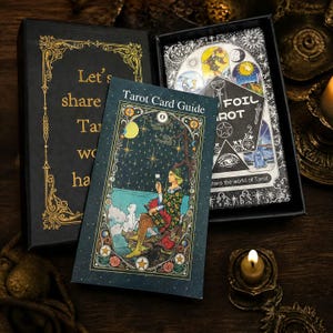 May include: A black box containing a deck of tarot cards and a guide booklet. The box lid features gold text reading Let's share the Tarot world. The guide booklet shows a figure with a dog by the sea under a starry sky. A small card reads Foil Tarot.