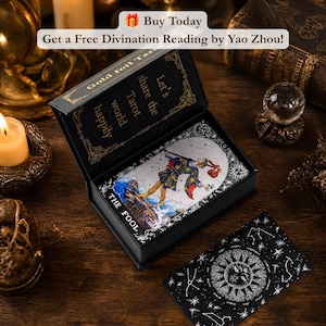 May include: A black box containing a tarot deck with the card titled The Fool visible, featuring a colorful figure on a cliff. The box lid interior reads Let's share the Tarot world happily. A separate card with a sun and star design lies nearby.