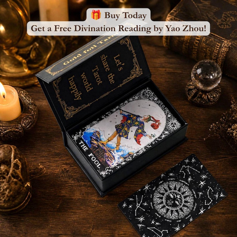 May include: A black box containing a tarot deck with the card titled The Fool visible, featuring a colorful figure on a cliff. The box lid interior reads Let's share the Tarot world happily. A separate card with a sun and star design lies nearby.