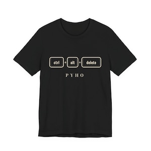 May include: A black short-sleeved t-shirt featuring a graphic print of three rectangular keys labelled ctrl, alt, and delete, separated by plus signs. Below the keys, the text PYHO is printed in a clean, light-coloured sans-serif font.