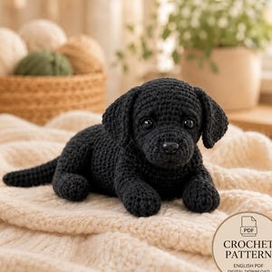 Può includere: Un giocattolo a forma di cane realizzato all'uncinetto nero con orecchie pendenti e occhi scuri, sdraiato su una coperta color crema testurizzata. Un badge circolare nell'angolo riporta il testo PDF CROCHET PATTERN ENGLISH PDF DIGITAL DOWNLOAD.