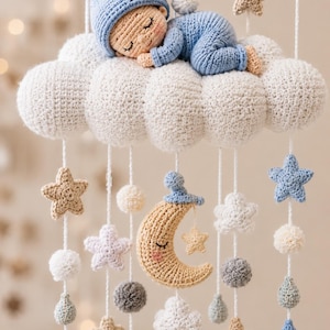 Puede incluir: Un móvil de ganchillo para bebé con una gran nube blanca y un bebé durmiendo con traje y gorro azules. De la nube cuelgan hilos blancos con estrellas beige, azules y blancas, pequeños pompones, formas de gota y una luna creciente.