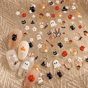 May include: A sheet of adhesive nail decals featuring Halloween motifs including black cats, white ghosts, orange pumpkins, mushrooms, acorns, witch hats, and white flowers. The center text reads Happy Halloween. Five decorated artificial fingernails are included.
