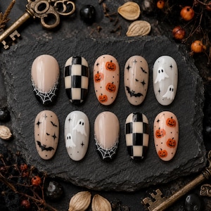 May include: A set of ten press-on nails featuring Halloween-themed designs including black and white spiderwebs, a black and white checkerboard pattern, orange jack-o'-lanterns, black bats with stars, and white ghosts on a neutral base.