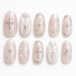 May include: A set of ten oval-shaped press-on nails with a pearlescent finish. The designs feature silver metallic crosses, white angel wings, silver star charms, small white pearls, and clear rhinestones arranged in various decorative patterns.