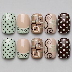 May include: A set of ten press-on nails arranged in two rows. The designs include light green with dark brown polka dots, nude with green circle accents, nude with brown and white squares, nude with brown and green swirls, and dark brown with light green dots.
