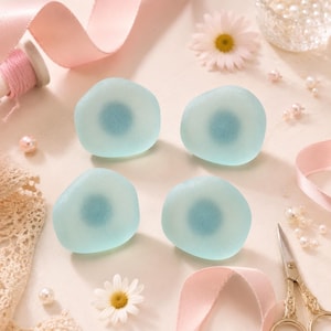 May include: Four smooth, rounded, translucent light blue glass cabochons with a darker blue circular center. These decorative pieces have a frosted, matte finish and are arranged in a square formation, showcasing a soft, uniform appearance.