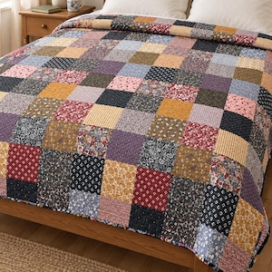 Könnte beinhalten: Eine Patchwork-Tagesdecke mit einem Raster aus quadratischen Stoffflicken in verschiedenen Farben wie Senfgelb, Marineblau, Dunkelrot und zartem Rosa. Die Quadrate zeigen verschiedene Blumen-, Vichy- und geometrische Muster mit sichtbaren Nähten.