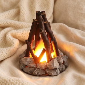 May include: A decorative campfire lamp featuring dark brown wooden twigs arranged in a conical shape over a bright orange glowing light, surrounded by a circular base of textured gray stones, creating a warm and realistic illumination effect.