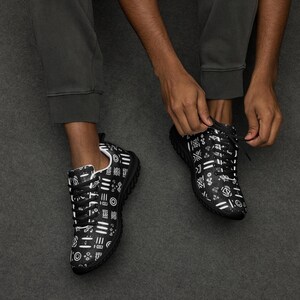 May include: A pair of black sneakers featuring a white geometric pattern of lines, circles, and abstract shapes. The shoes have black laces, a black sole, and a white interior lining. The pattern covers the entire upper portion of the footwear.