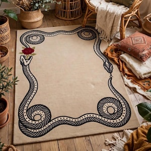 Può includere: Un tappeto rettangolare color beige chiaro con un bordo a linee nere raffigurante due serpenti intrecciati. Un serpente tiene in bocca una singola rosa rossa con foglie verdi. Il design è simmetrico con le code dei serpenti arrotolate.