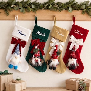 May include: Four velvet Christmas stockings in white, dark green, gold, and red, each featuring a personalised name embroidered on the cuff, a large fabric bow, and a decorative gnome ornament with a faux fur beard attached to the front.