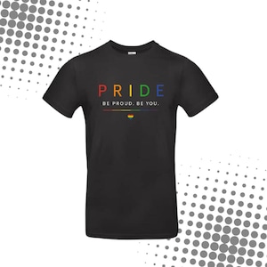 Könnte beinhalten: Ein schwarzes kurzärmeliges T-Shirt mit dem Wort PRIDE in Regenbogenfarben, dem weißen Text BE PROUD. BE YOU., einer dünnen horizontalen Regenbogenlinie und einem kleinen, regenbogenfarbenen Herzsymbol, das unter dem Text auf der Brust zentriert ist.