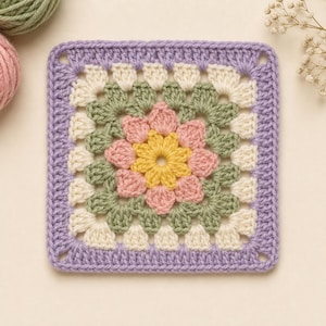 May include: A square crochet granny square featuring a central yellow flower motif surrounded by layers of pink, sage green, and cream yarn, finished with a solid lavender purple border. The intricate needlework displays a floral pattern.