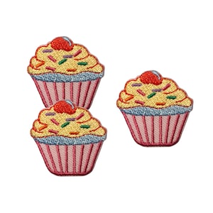 May include: Three embroidered cupcake patches featuring yellow frosting, a red cherry on top, and colorful sprinkles. Each cupcake has a light blue border and a pink pleated paper liner with vertical lines, rendered in detailed thread work.