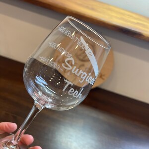 May include: A clear glass wine glass with the text "Surgical Tech" and a small illustration of a scalpel etched into the side.