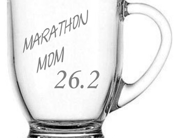 May include: Clear glass coffee mug with a handle. The mug has the text "Marathon Mom 26.2" etched on the side.