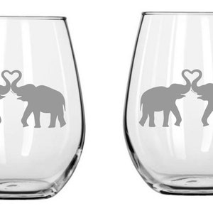 May include: Two clear glass wine glasses with a design of two elephants with their trunks intertwined to form a heart shape.