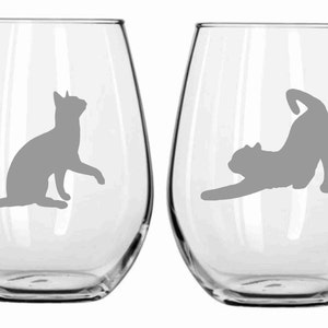 May include: Two clear glass wine glasses with a gray cat silhouette on each. One cat is sitting and the other is stretching.