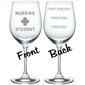 May include: Two clear glass wine glasses with a white design. The front glass says "Nursing Student" with a white plus sign. The back glass says "Don't even ask", "Rough day", and "Easy day".