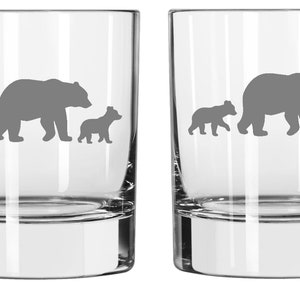 May include: Set of two clear glass tumblers with a design of a mama bear and two cubs walking in a line. The bears are gray and etched into the glass.