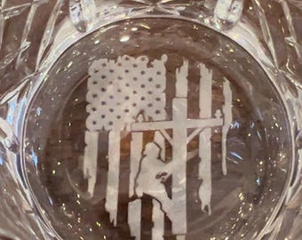 May include: A clear glass with an etched design of an American flag and a lineman working on a power line.