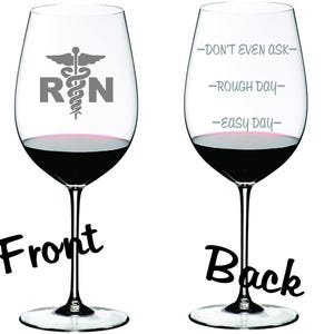 May include: A clear wine glass with a black and white image of a medical caduceus and the letters "RN" on the front. The back of the glass has the text "Don't even ask", "Rough day", and "Easy day" printed on it.