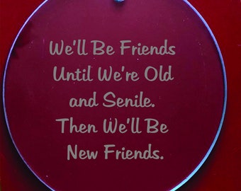 May include: A round, burgundy-colored ornament with the text "We'll Be Friends Until We're Old and Senile. Then We'll Be New Friends." in a light gray font. The ornament has a silver string for hanging.