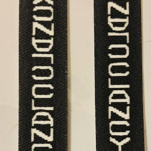 May include: Two rectangular black fabric labels with white embroidered text. The text on the left label reads XOZDROUZO in a vertical orientation, while the right label features the same text in a mirrored or inverted vertical orientation.