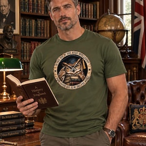Può includere: Una t-shirt a maniche corte color verde oliva con una grafica circolare raffigurante un gufo con occhiali e tocco di laurea, appoggiato su una pila di libri. Il testo attorno al gufo recita: "JE SAIS QUE JE SUIS ASSEZ INTELLIGENT POUR SAVOIR QUE JE NE SUIS PAS ASSEZ."